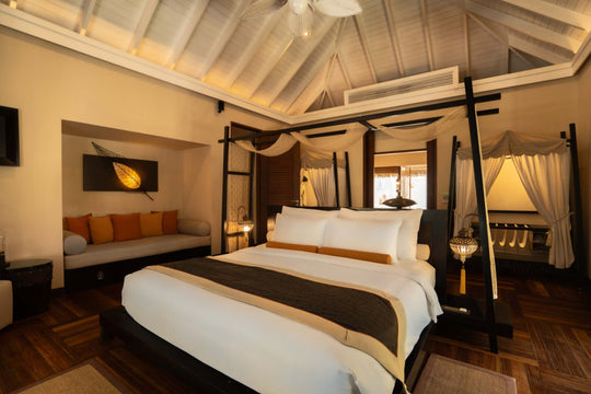 A four poster bed at Ayada Maldives flanked by two nightstands under a timber ceiling