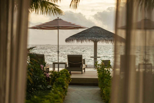 Sun Siyam Olhuveli, South Malé Atoll — view from inside a Beach Pavilion to a thatched parasol and loungers on the sand