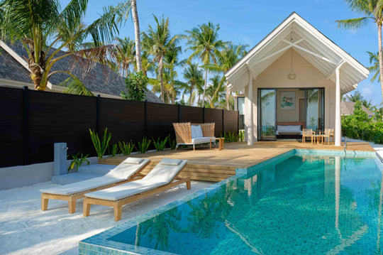 A Beach Villa at ananea Madivaru Maldives from across the pool, sun loungers on the deck and palms behind
