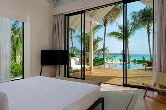 A Beach Villa bedroom at ananea Madivaru Maldives looking out through glass to the terrace and the sea