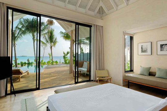 A Beach Villa bedroom at ananea Madivaru Maldives with a window seat and the beach through the glazed wall