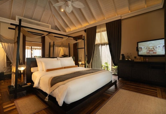 A Beach Villa bedroom at Ayada Maldives, bed and television under a pitched white ceiling
