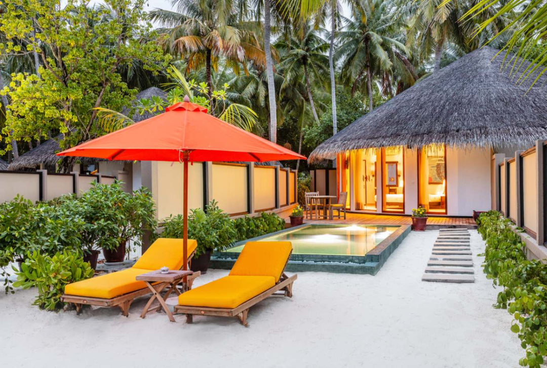Angsana Velavaru, Dhaalu Atoll — the villa pool lit at dusk, with a red parasol, loungers and the thatched roof behind