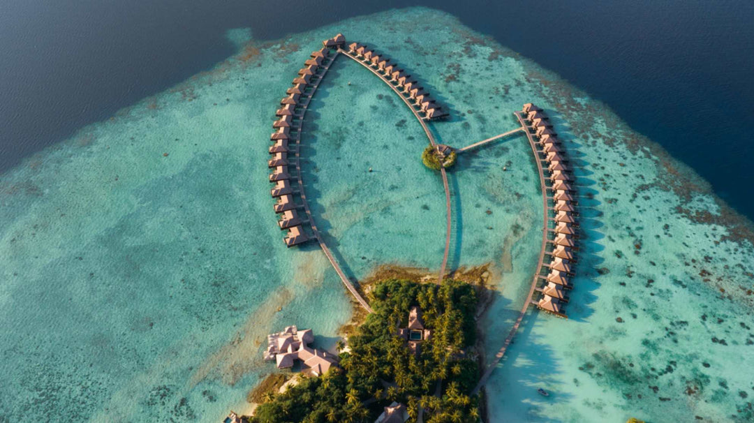 Aerial view of Ayada Maldives, the overwater villas reaching out over pale reef into deeper water