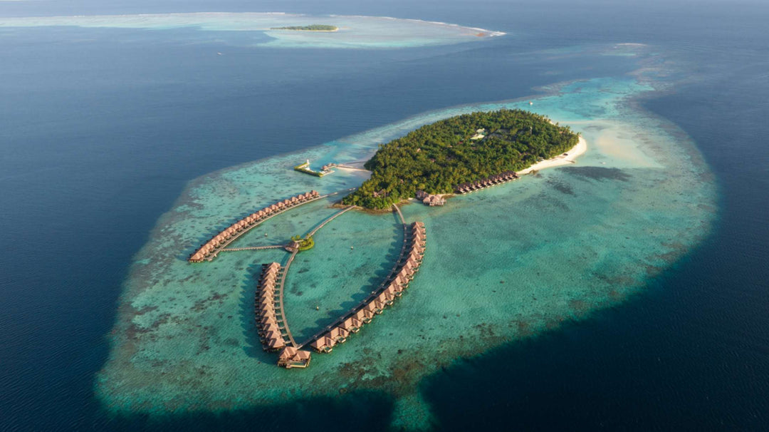 Ayada Maldives from the air, reef patterns visible through clear water around the overwater villas