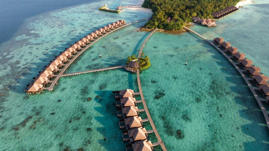 Ayada Maldives from the air, the overwater villas in two lines above bright turquoise shallows