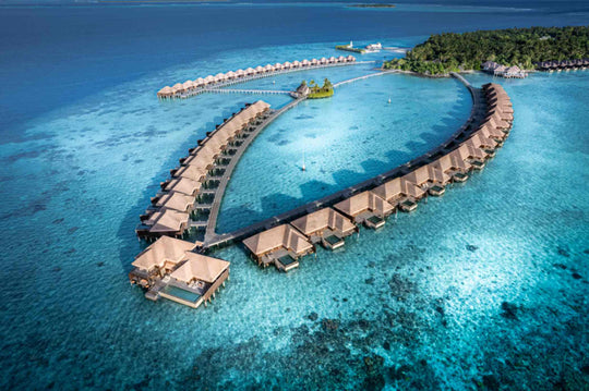 Ayada Maldives from the air, the overwater villas curving away over the reef flat