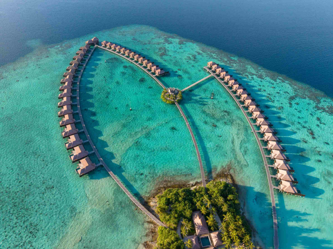 Ayada Maldives from the air, the full loop of overwater villas beside the wooded island