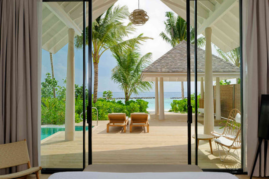 Sun loungers under a shaded pavilion at a beach villa at ananea Madivaru Maldives, the sea beyond the palms