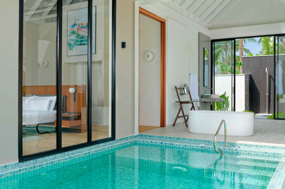 A beach villa at ananea Madivaru Maldives seen across the pool, the bathroom and bedroom behind the glass