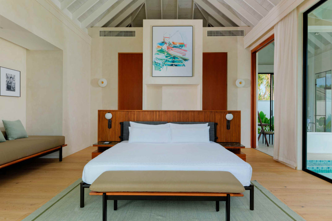 A beach villa bedroom at ananea Madivaru Maldives, the bed against a timber panelled wall under a framed print