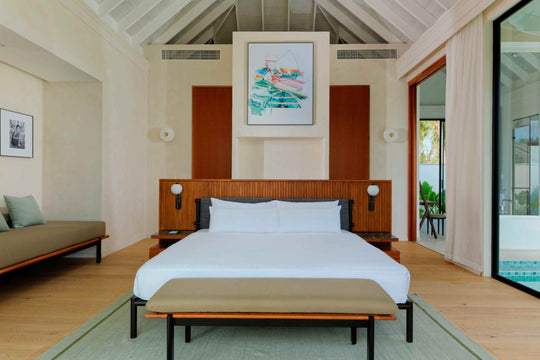 A beach villa bedroom at ananea Madivaru Maldives, the bed against a timber panelled wall under a framed print