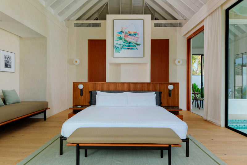 A beach villa bedroom at ananea Madivaru Maldives, the bed against a timber panelled wall under a framed print