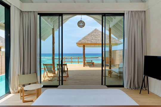 The view from inside an overwater villa at ananea Madivaru Maldives, through the open doors to the deck and the sea