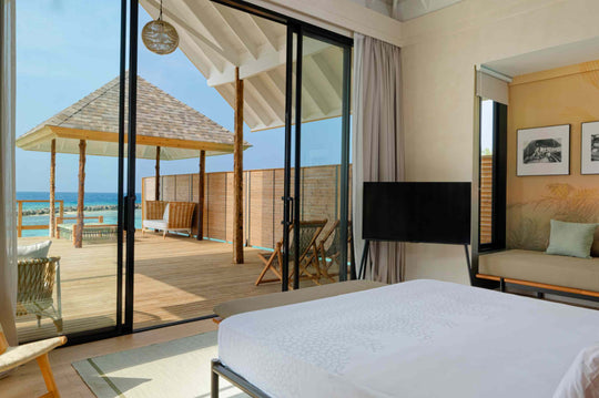 A villa bedroom at ananea Madivaru Maldives opening on to a shaded deck and the sea