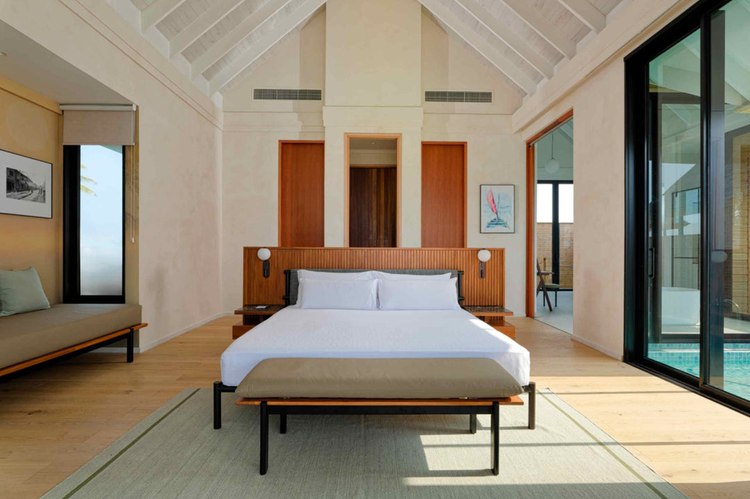 A villa bedroom at ananea Madivaru Maldives, bed against a panelled wall with a bench at its foot