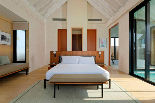 A villa bedroom at ananea Madivaru Maldives, bed against a panelled wall with a bench at its foot