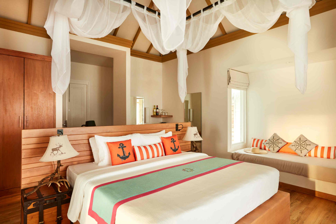 Sun Siyam Iru Veli, Dhaalu Atoll — bedroom with a four-poster bed and muslin drapes, orange anchor cushions and a daybed