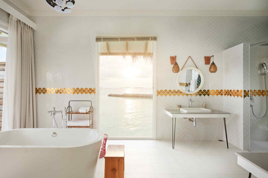 Sun Siyam Iru Veli, Dhaalu Atoll — overwater bathroom, a freestanding tub facing an open doorway onto the lagoon at sunset