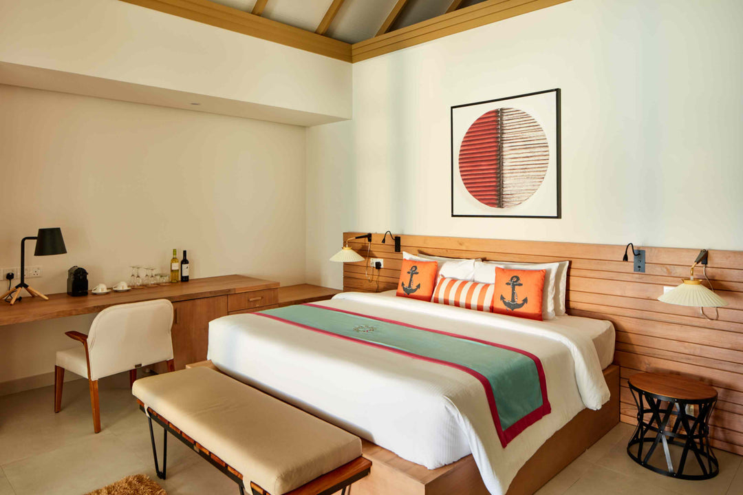 Sun Siyam Iru Veli, Dhaalu Atoll — bedroom with a timber headboard, orange anchor cushions, desk and bench