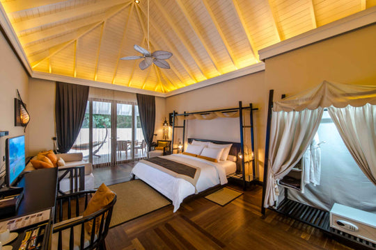 A garden villa bedroom at Ayada Maldives, four poster bed with drapes under a warm timber roof