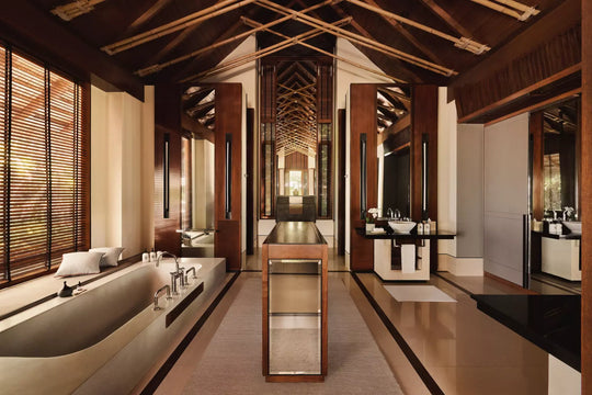 Bathroom of a One&amp;Only Reethi Rah Grand Beach Villa, with a long stone bath, twin vanities and louvred shutters under a pitched timber ceiling