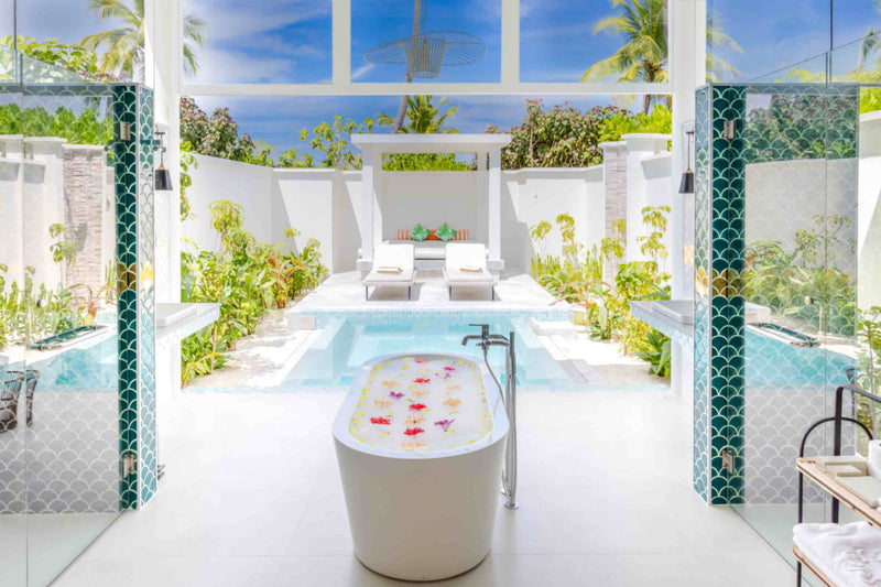 An open-air bathroom at Sun Siyam Iru Veli looking through to a private pool and loungers, with a flower-strewn tub.