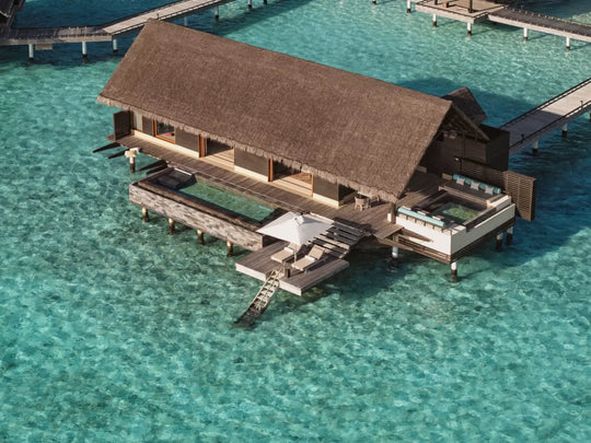 Aerial view of a One&amp;Only Reethi Rah Grand Water Villa with Pool on stilts above the turquoise lagoon, its infinity pool running the length of the deck