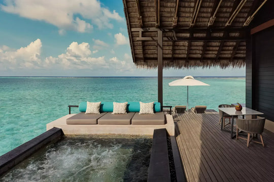 Overwater deck of a One&amp;Only Reethi Rah Grand Water Villa, with a jacuzzi, a cushioned daybed and a dining table facing the open sea