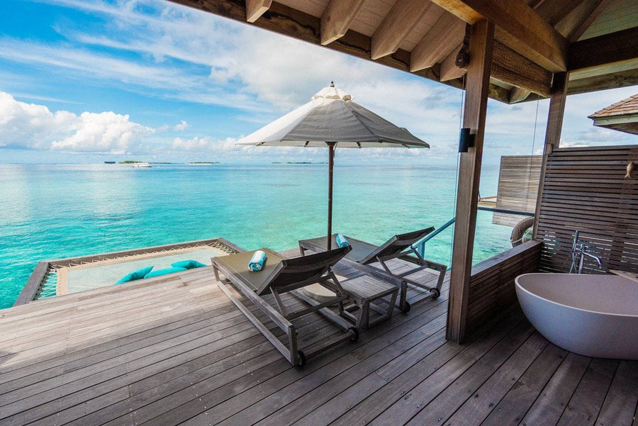 An overwater villa deck at Hurawalhi Maldives with loungers, a freestanding bath and a net hammock suspended over the lagoon.