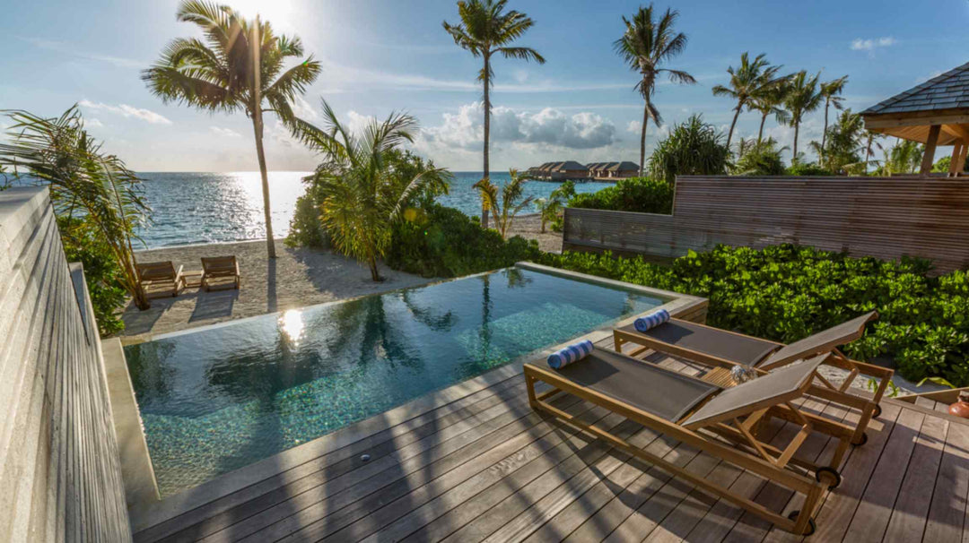Hurawalhi Maldives, Lhaviyani Atoll — late afternoon sun on a beach villa pool and timber deck, the overwater villas visible along the reef