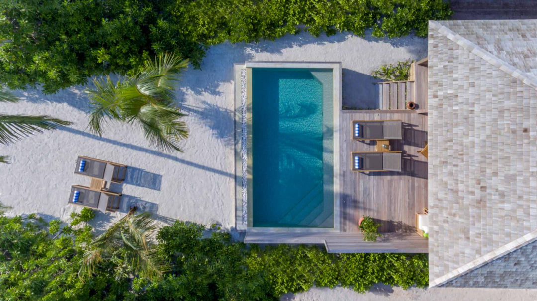Hurawalhi Maldives, Lhaviyani Atoll — a beach villa from directly overhead: pool, timber deck, shingle roof and palm shadows on white sand