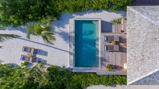Hurawalhi Maldives, Lhaviyani Atoll — a beach villa from directly overhead: pool, timber deck, shingle roof and palm shadows on white sand