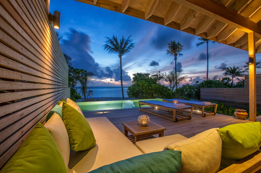 Hurawalhi Maldives, Lhaviyani Atoll — a villa terrace at dusk, lanterns lit on the deck and the pool glowing green against a violet sky