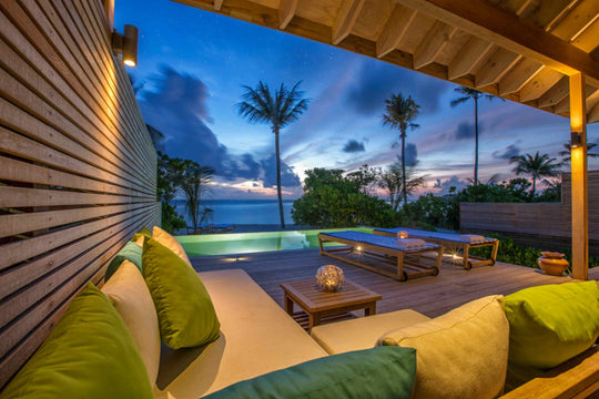 Hurawalhi Maldives, Lhaviyani Atoll — a villa terrace at dusk, lanterns lit on the deck and the pool glowing green against a violet sky