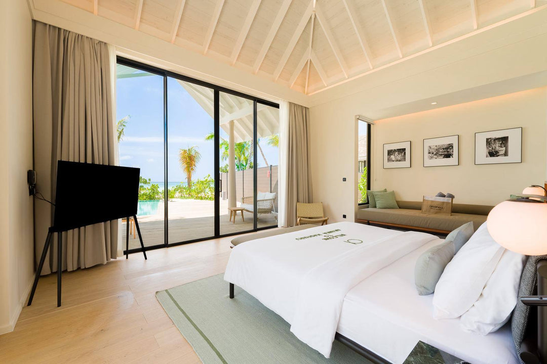 A villa bedroom at ananea Madivaru Maldives with the television facing the bed and the garden beyond the glass