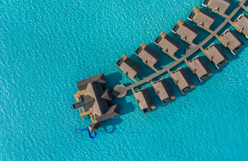 Rows of overwater villas curving out across the turquoise lagoon at JW Marriott Maldives Kaafu Atoll, seen from directly above