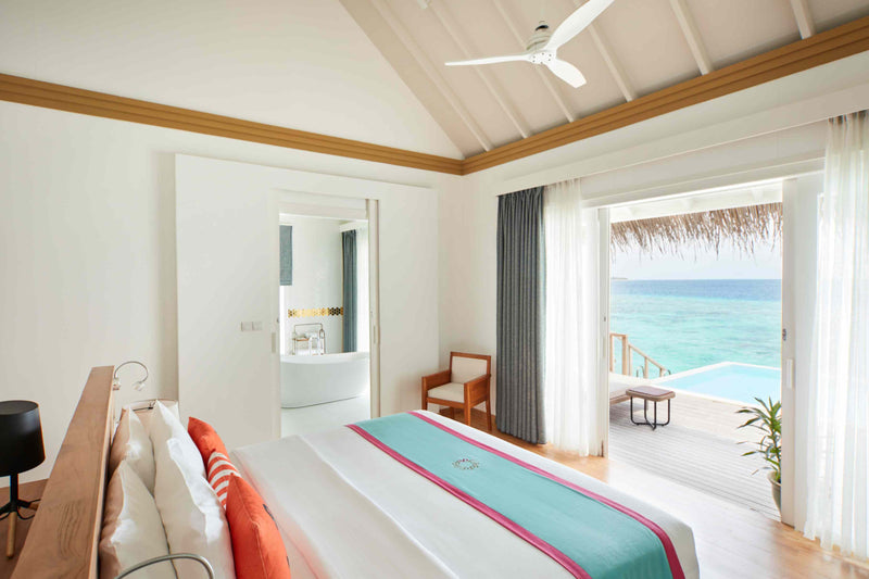 An overwater bedroom at Sun Siyam Iru Veli with doors open to the deck, pool and lagoon.