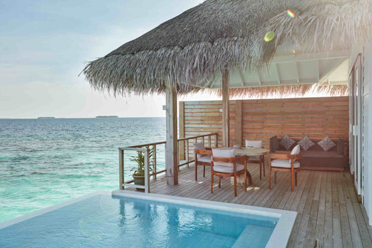 Sun Siyam Iru Veli, Dhaalu Atoll — overwater villa deck under a thatched roof, dining table and sofa beside the private pool