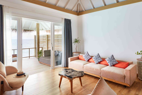 Sun Siyam Iru Veli, Dhaalu Atoll — overwater living room with a sofa in coral cushions and doors to the deck