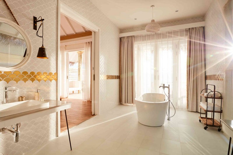 A bathroom at Sun Siyam Iru Veli with a gold fish-scale tile band, tub and twin basin, bedroom beyond.