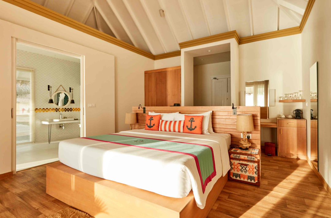 Sun Siyam Iru Veli, Dhaalu Atoll — bedroom in warm timber with orange anchor cushions, a desk and the ensuite beyond