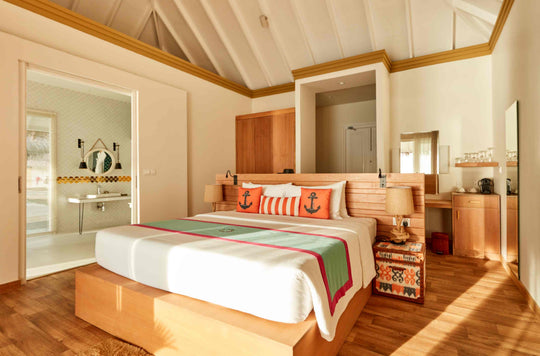 Sun Siyam Iru Veli, Dhaalu Atoll — bedroom in warm timber with orange anchor cushions, a desk and the ensuite beyond