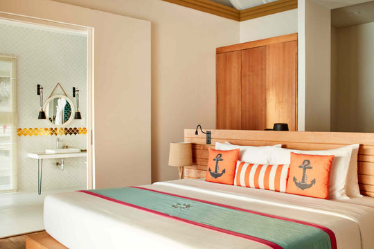 Sun Siyam Iru Veli, Dhaalu Atoll — bedroom with a timber wardrobe wall, orange anchor cushions and the ensuite through the door
