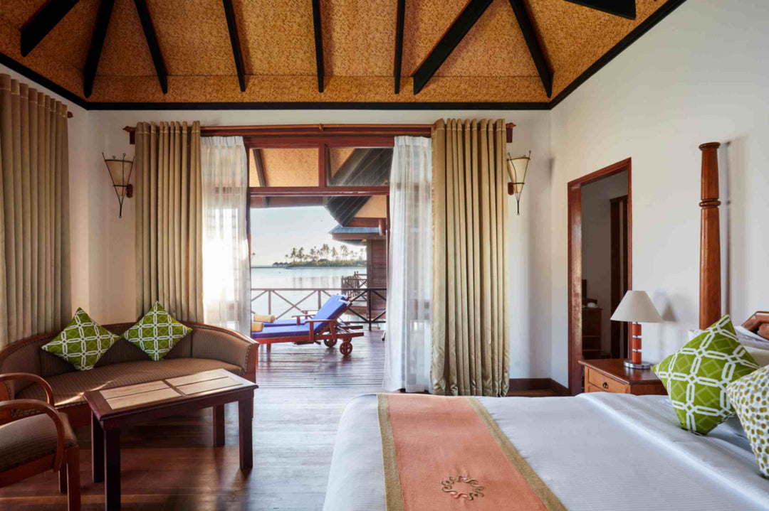 Sun Siyam Olhuveli, South Malé Atoll — water villa bedroom looking out past the sofa to the deck and the lagoon