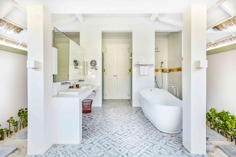 A suite bathroom at Sun Siyam Olhuveli with a freestanding bath, twin basins and patterned floor tiles.