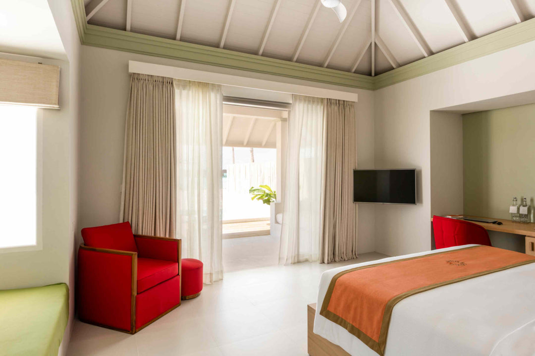 Sun Siyam Olhuveli, South Malé Atoll — beach villa bedroom with a red armchair and doors to the terrace