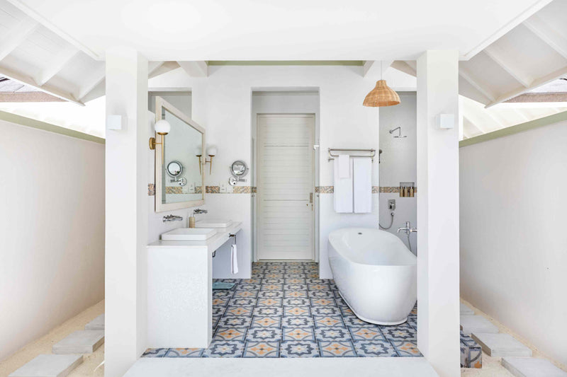 A bathroom at Sun Siyam Olhuveli with patterned floor tiles, a freestanding bath and twin basins.