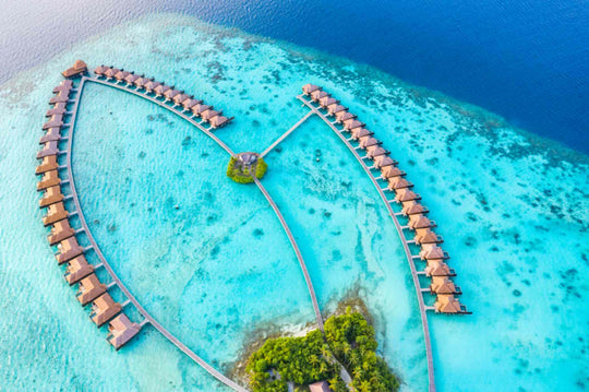 Both arms of overwater villas at Ayada Maldives from directly overhead, meeting at a small islet