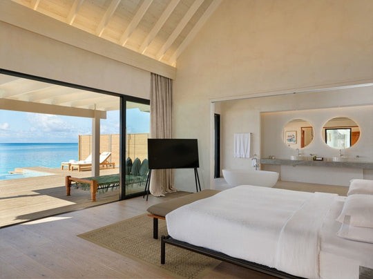 A villa bedroom at ananea Madivaru Maldives with the bathroom behind and the sea through the open doors
